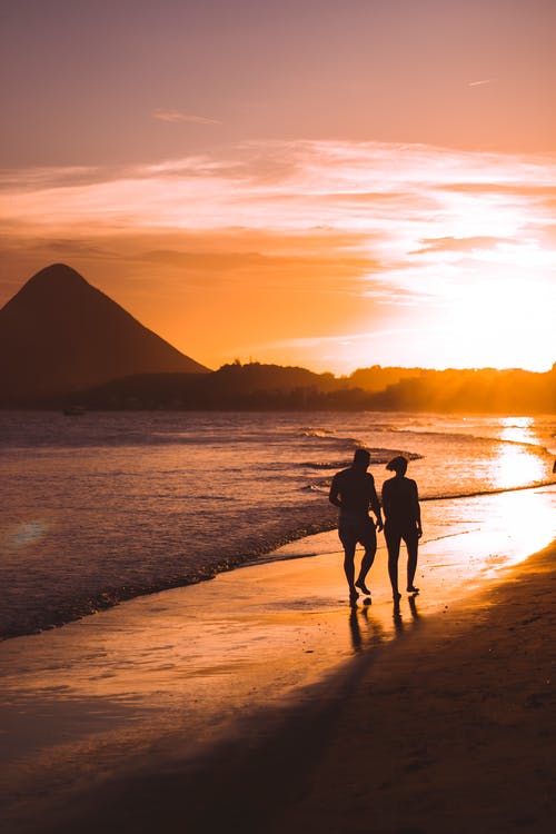 silhouette of two people walking on beach at sunset