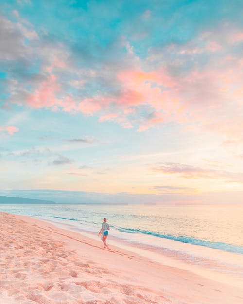 woman in sweatshirt walking on white beach during sunset